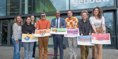 Vertegenwordigers van paternerorganisaties staan met de logo's van hun organisatie buiten een fysieke meldpunt